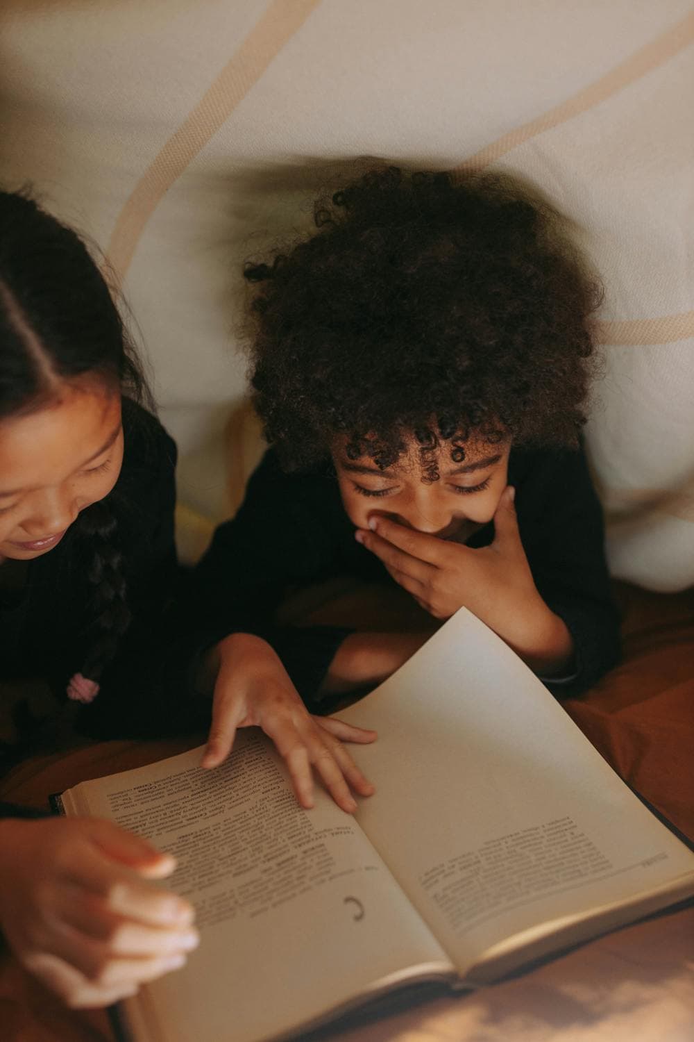 Two kids reading a book together in a cozy dimly lit tent